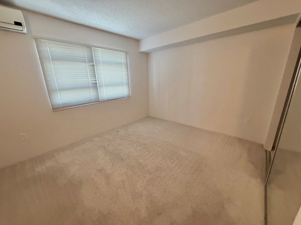 A room with a window covered by blinds and a carpet on the floor.
